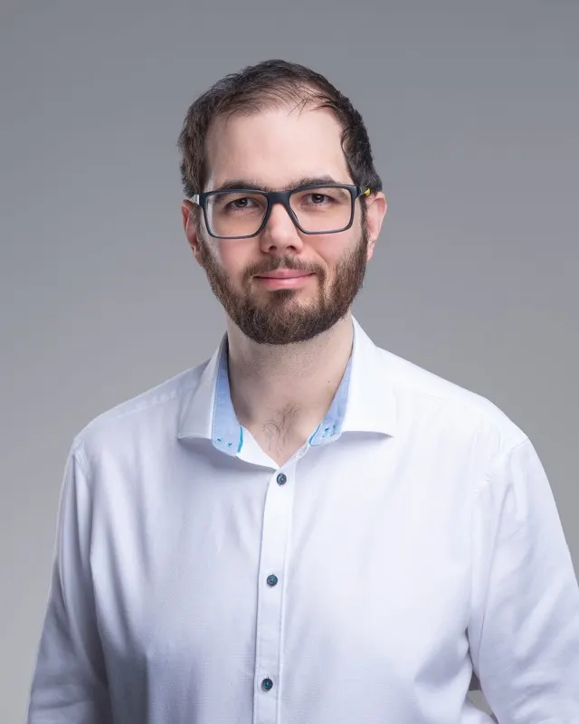 Ágoston Zajkás fehér ingben, szürke háttér előtt, portré